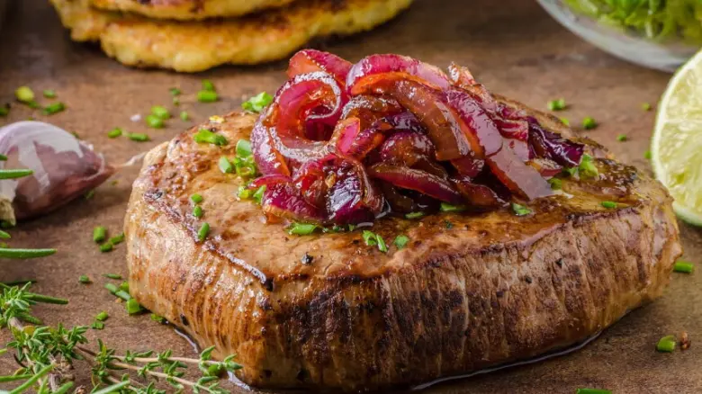 Steak s karamelizovanou cibulí na dřevěném podkladu.