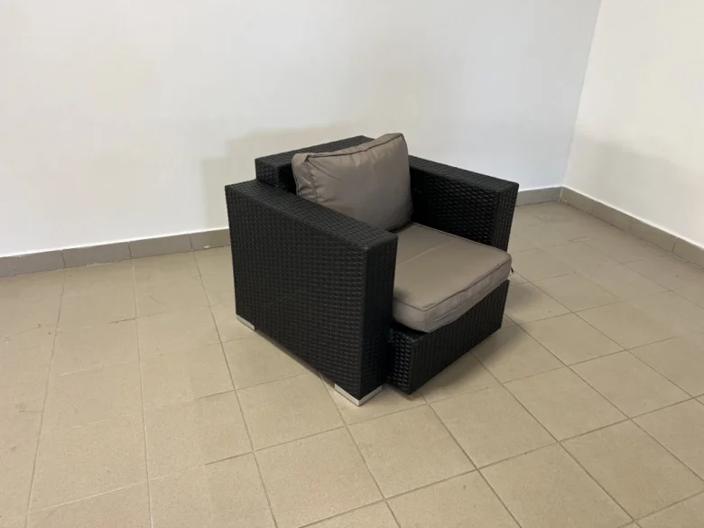 Černé ratanové křeslo s polštáři v prázdném pokoji.