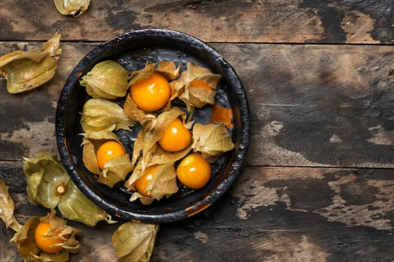 Čerstvé plody physalis v tmavé misce na dřevěném povrchu.