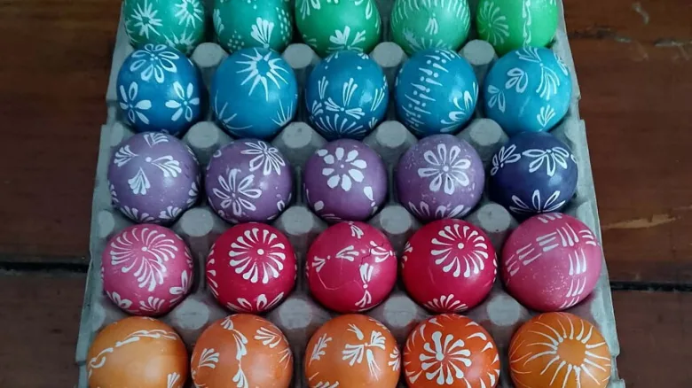 Různobarevná vajíčka namalovaná bílým vzorem na kartonu.