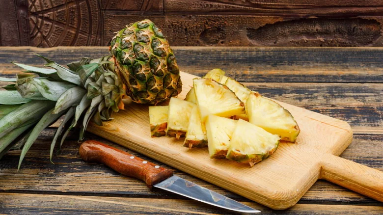 Celý ananas s nakrájenými kousky na dřevěném prkénku.
