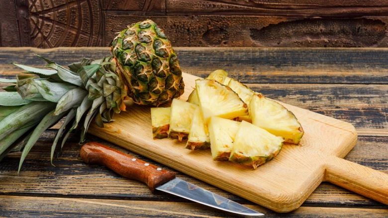 Celý ananas s nakrájenými kousky na dřevěném prkénku.
