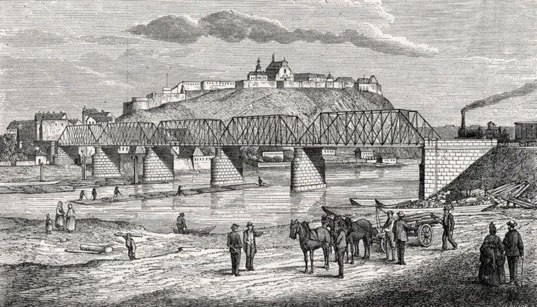 Historický železniční most v Praze s pevností na kopci.