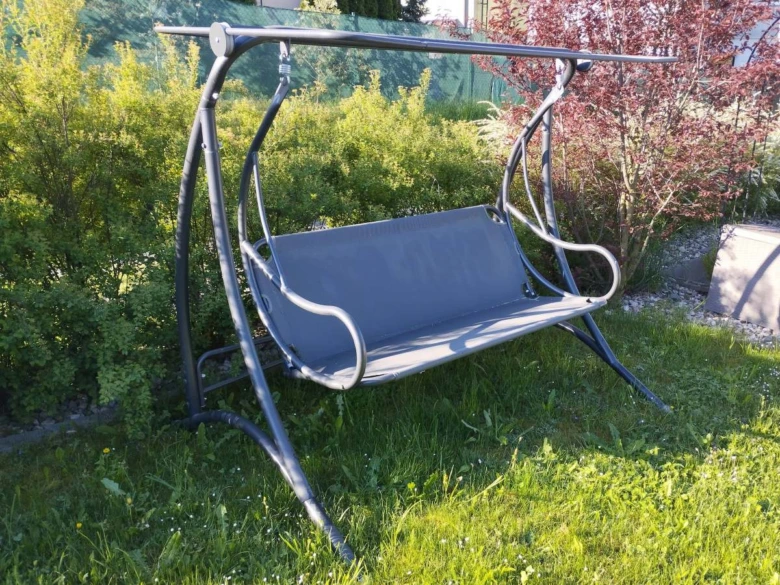 Zahradní houpačka na sedák z tmavého kovu v trávě.