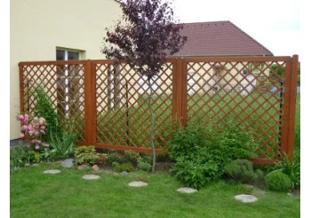 Dřevěný plot s mřížovými panely v zahradním prostředí.