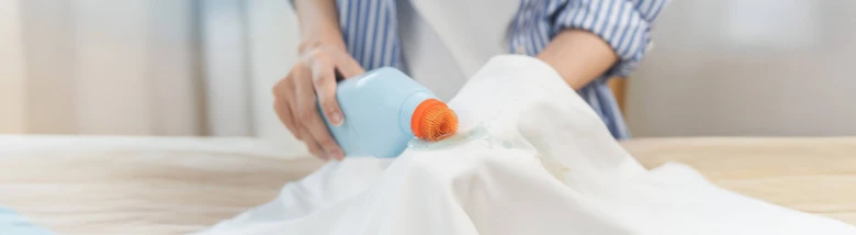 Člověk nalévá tekutinu z modré lahvičky na bílý textil.