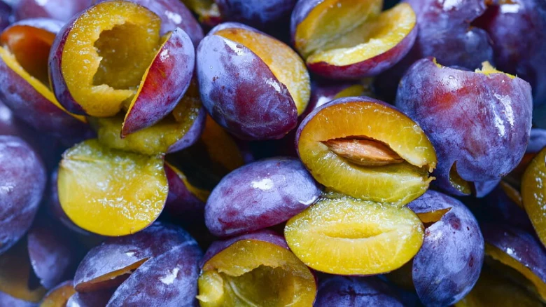 Čerstvé švestky nakrájené na půlku s viditelnou dužinou a jádrem.