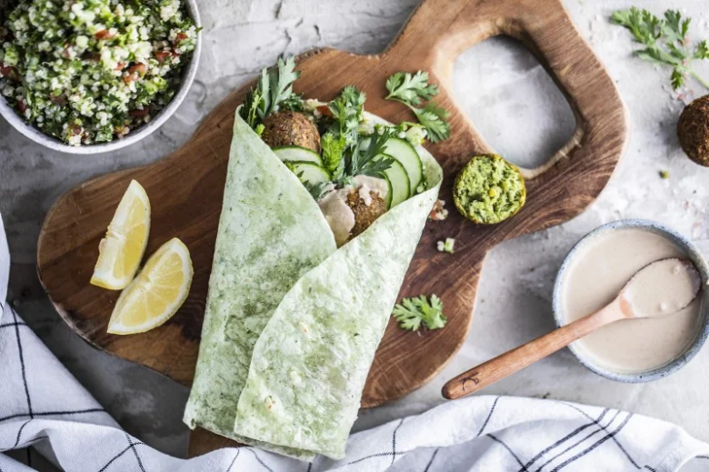 Falafel sýrová rolka se zeleninou a omáčkami na dřevěném talíři.