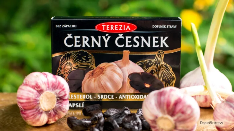 Krátký záběr na krabičku černého česneku s čerstvými hlavičkami a loupkami.