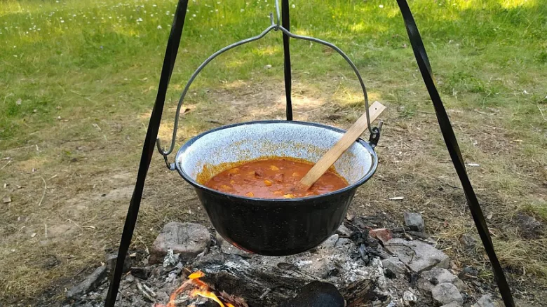 Kotlík s polévkou visí nad ohněm venku.