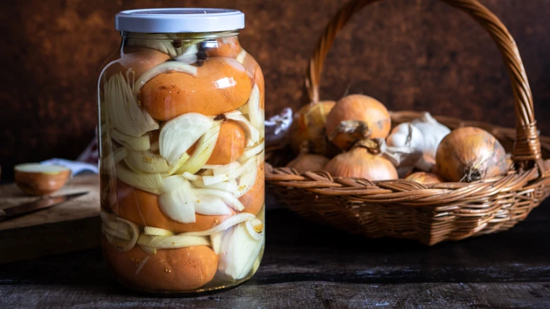 Sklenice s utopenými cibulí a mrkví vedle košíku čerstvé cibule.