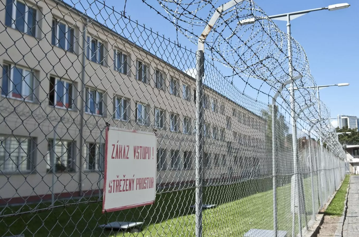 Ohradní plot věznice v Praze-Pankráci s výstražným štítem.