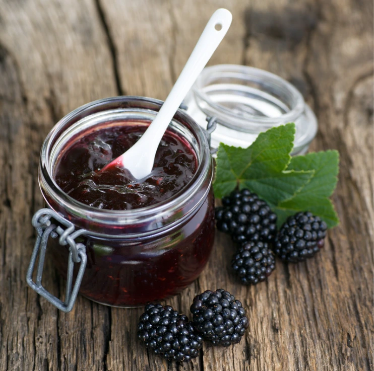 Sklenice ostružinové marmelády s čerstvými plody na dřevě.