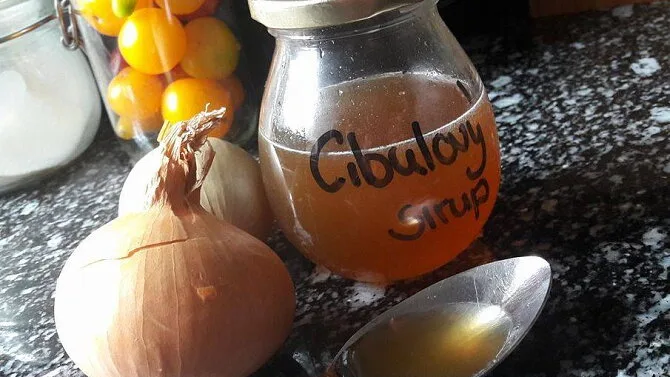Sklenice cibulového sirupu s čerstvými cibulemi na kuchyňské desce.