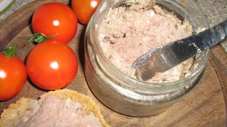Domácí paštika v sklenici s rajčaty na dřevěném talíři.