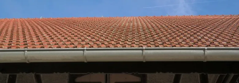 Červená střecha s nainstalovaným bílým okapem na domě.
