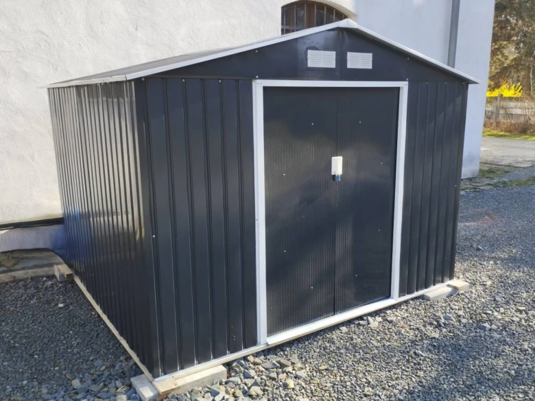 Černý zahradní domek bez stavebního povolení na štěrkové ploše.
