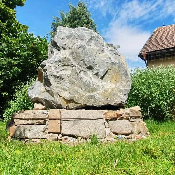 Velký přírodní balvan na kamenném podstavci v zahradě.
