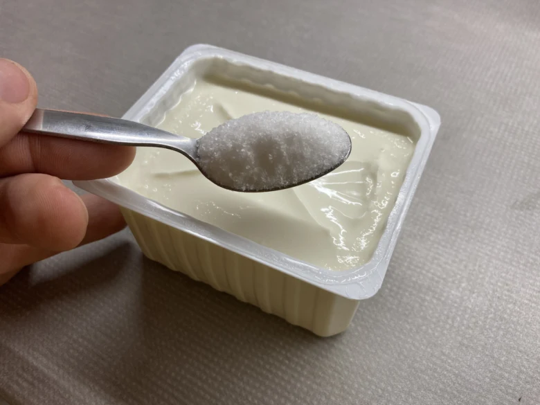 Lžíce s cukrem nad fermentovaným tvarohem v kelímku