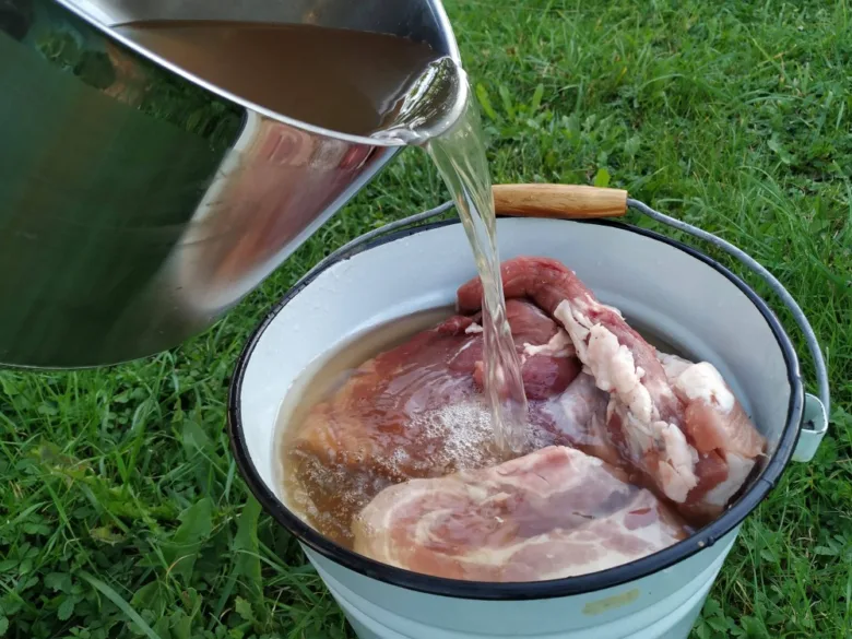 Nalévání masa solným roztokem do kbelíku venku.