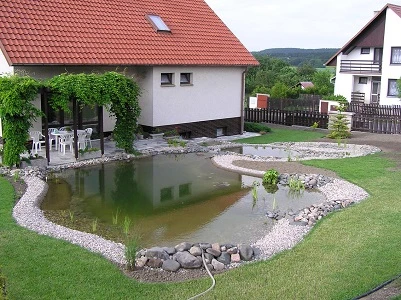 Přirozené koupací jezírko v zahradě s rostlinami a kamením.