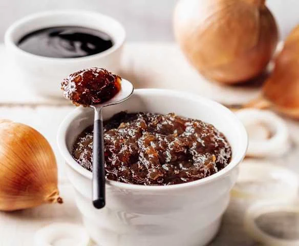Červená cibulová chutney v bílé mísce s lžící.