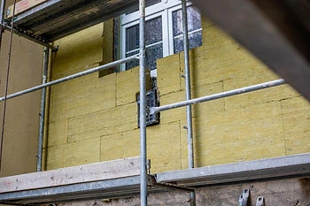 Žlutá skelná vata na fasádě budovy pod instalací s konstrukcí.