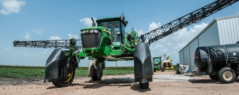 Zelený traktor s rozprašovačem pro péči o bavlnu.