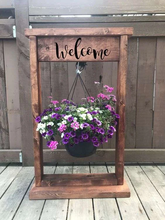 Dřevěný stojan na květinu s nápisem Welcome.