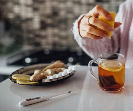 Člověk stlačuje citron do čaje s ingvem pro domácí léčbu.