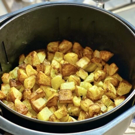 Zlatohnědé pečené brambory v košíku horkovzdušné fritézy.