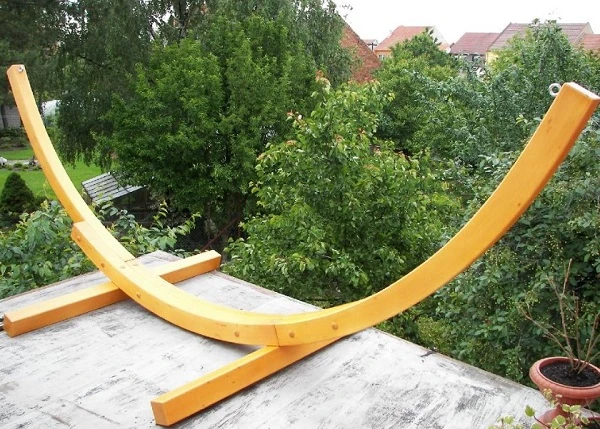 Žlutý dřevěný rám houpačky na zahradu před keři.