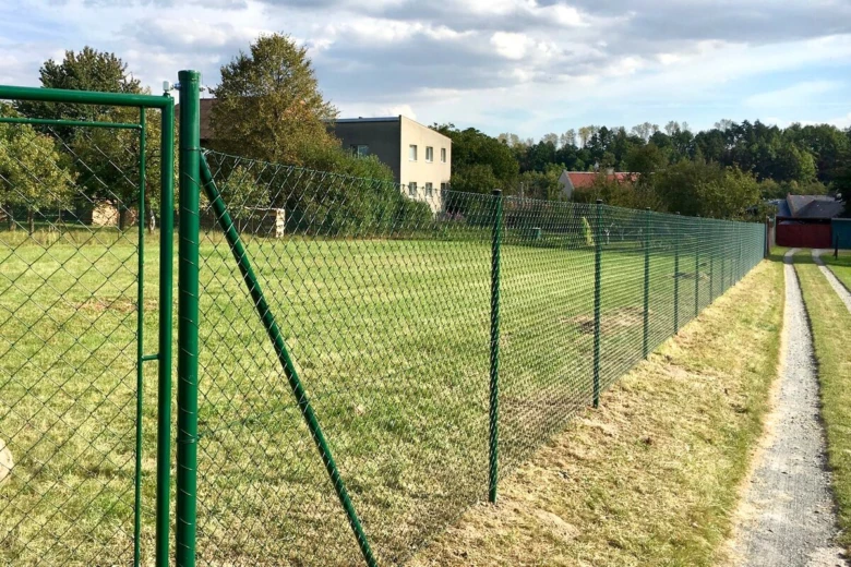 Zelený drátěný plot na trávníku vedle cestičky.