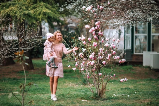 Žena s dítětem stojí u kvetoucího keře magnolie v zahradě.