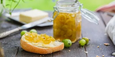 Kousek chleba s džemem z angreštu vedle sklenice.