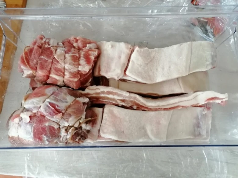 Surové kousky krkovice v plastové nádobě před uzením doma.