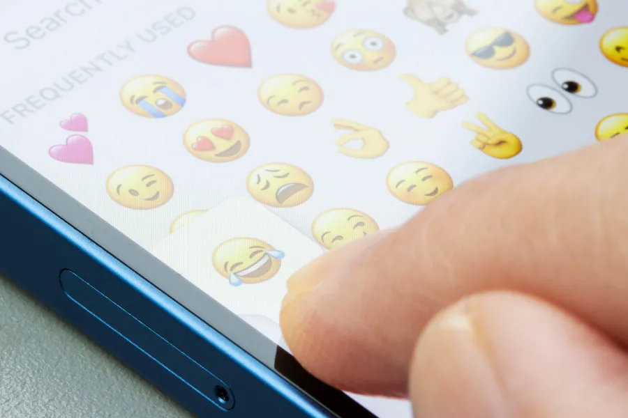 Finger selecting thumbs-up emoji on phone screen