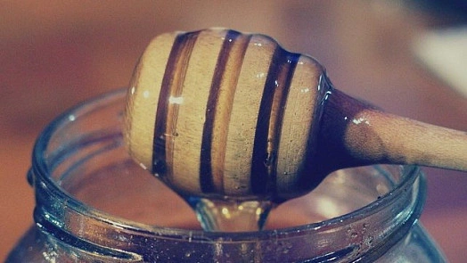 Dřevěný lžíce s medem kape do sklenice.