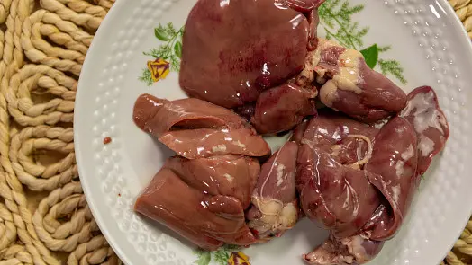 Surové játra a srdce na bílém talíři pro domácí paštiku.