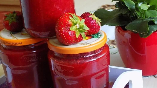 Sklenice domácí jahodové marmelády s čerstvými jahodami.