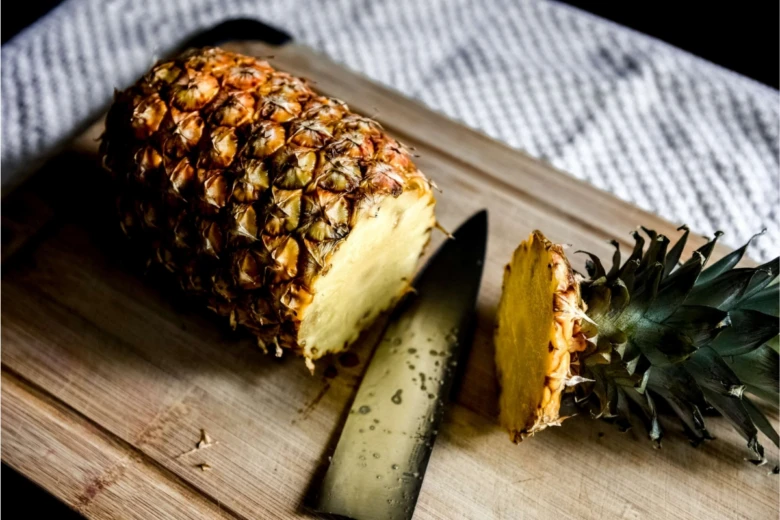 Ananas nakrájený na dřevěném prknu s nožem.