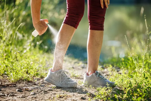 Person applying repellent spray to legs outdoors