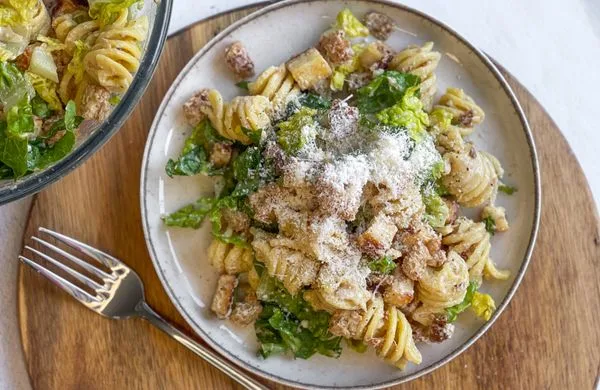 Pasta salát s listím zeleninou a strouhaným sýrem na talíři.
