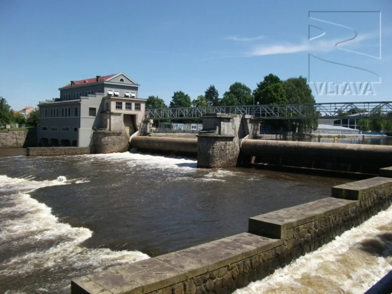 Vltavská přehradní stavba s budovou na břehu řeky.