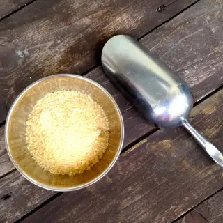 Miska s cukrem vedle lžíce na dřevěném povrchu.