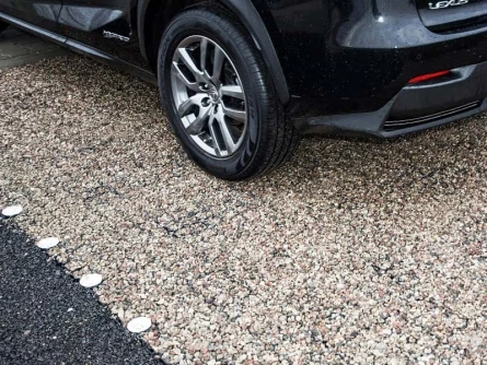 Černé auto stojí na štěrkové příjezdové cestě.