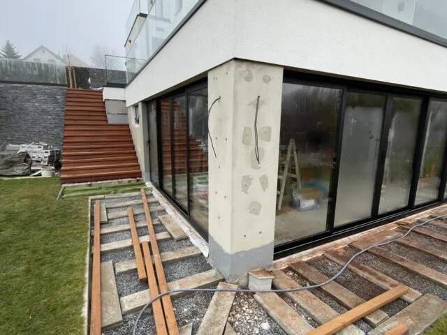 Stavba terasy s dřevěnými trámy u domu se skleněnou fasádou.