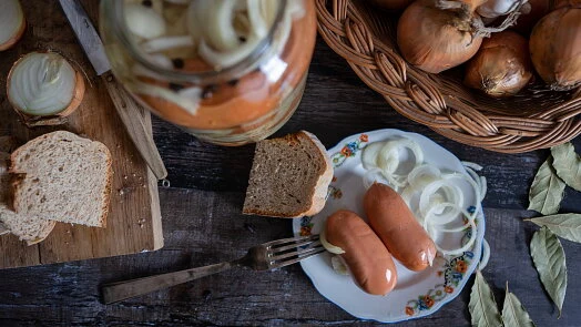 Sklenice nakládané cibule s uzeninou na tmavém dřevěném stole.