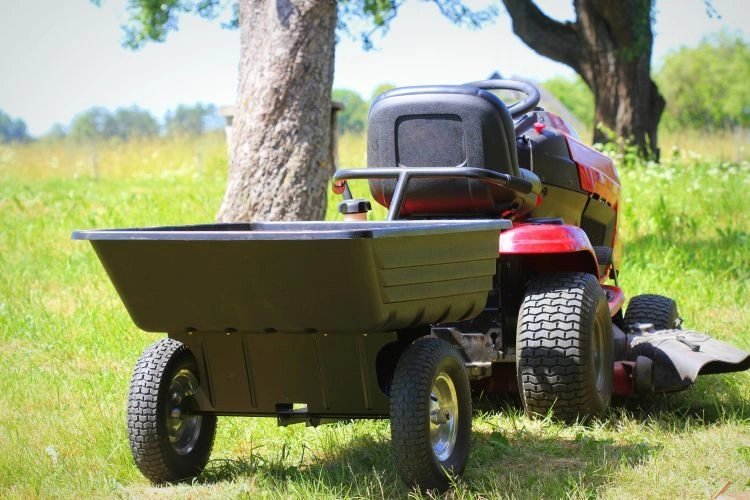 Červený traktor na trávu s přívěsem pro údržbu zahrady.