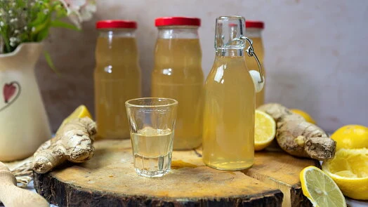 Sklenice s domácí zázvorovou limonádou vedle čerstvého zázvoru a citronů.